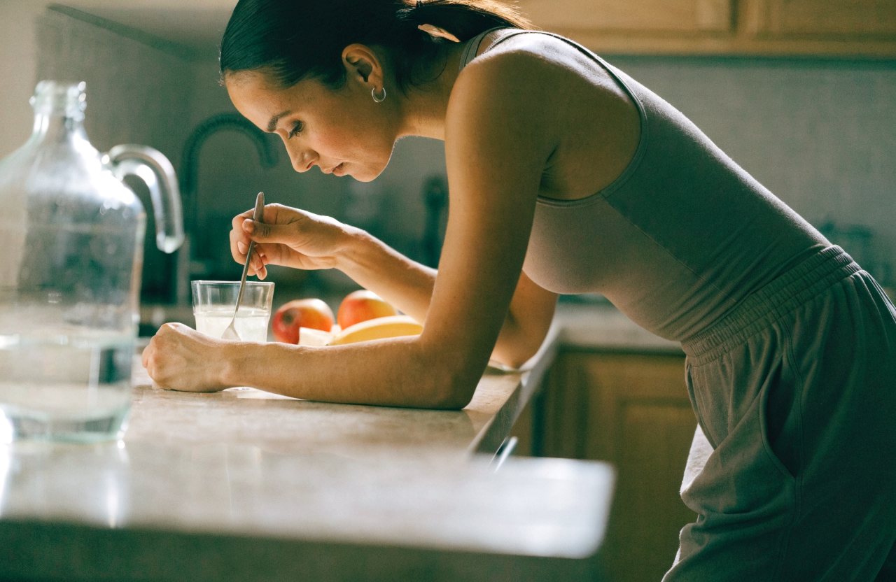 A woman stirring a drink mix into a glass of water at a kitchen counter